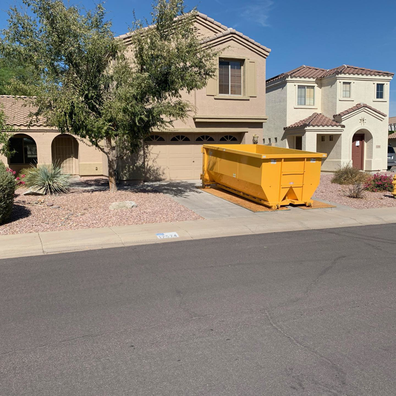 A yellow dumpster placed in a residential driveway for junk removal by AZ Dumpster Rentals in Surprise, AZ