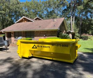 A yellow Delta Waste Solutions dumpster placed in a residential driveway for junk removal in Hattiesburg, MS.