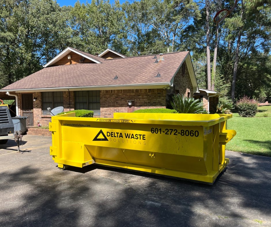 A yellow Delta Waste Solutions dumpster placed in a residential driveway for junk removal in Hattiesburg, MS.