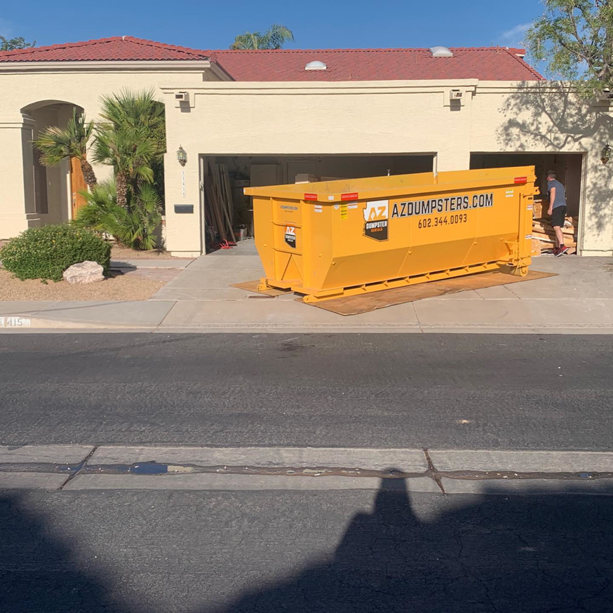 A yellow dumpster placed in a residential driveway with a person loading it for AZ Dumpster Rentals in Surprise, AZ