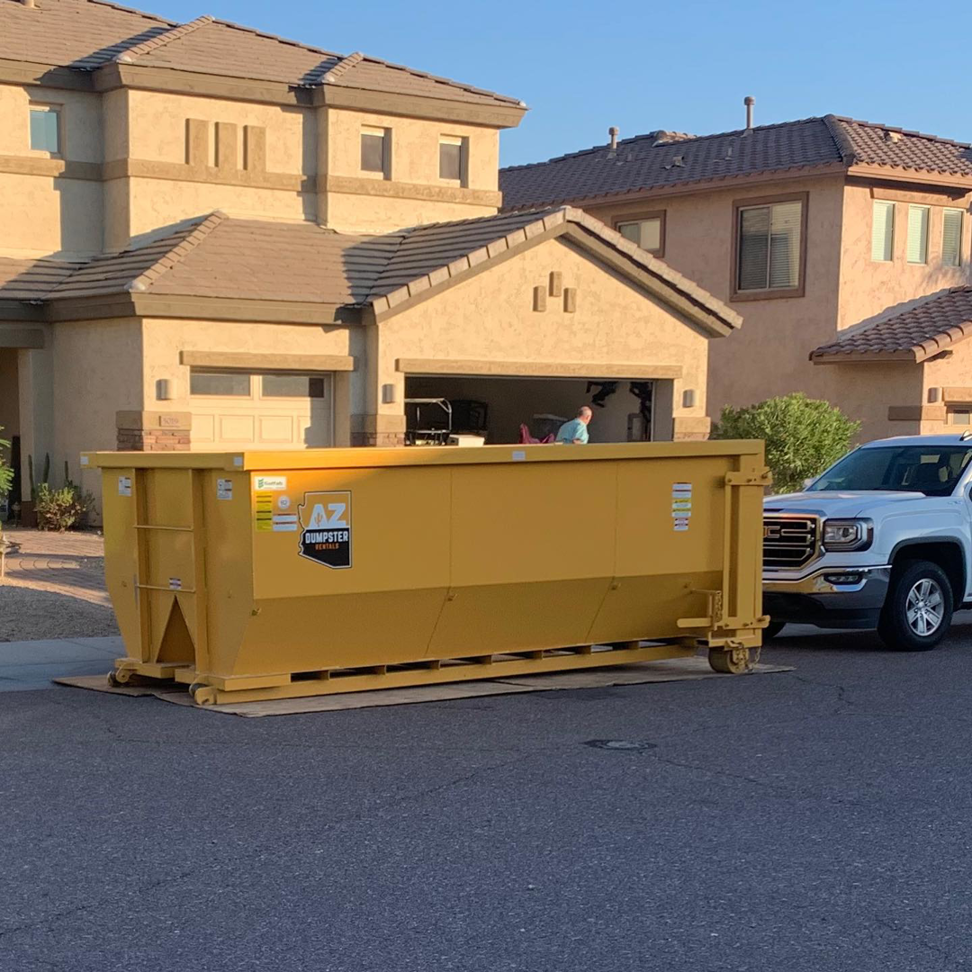 A yellow dumpster placed in front of a residential garage with a person loading it for AZ Dumpster Rentals in Surprise, AZ