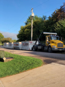 A yellow roll-off truck transporting multiple white dumpsters for Kuchel Roll-Offs in Sioux City, IA.