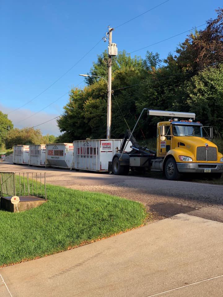 A yellow roll-off truck transporting multiple white dumpsters for Kuchel Roll-Offs in Sioux City, IA.