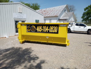 A bright yellow roll-off dumpster placed on a gravel lot by Tecumseh Rolloff Services in Moore, OK.
