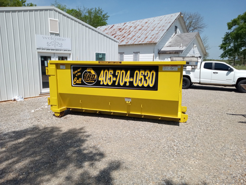 A bright yellow roll-off dumpster placed on a gravel lot by Tecumseh Rolloff Services in Moore, OK.