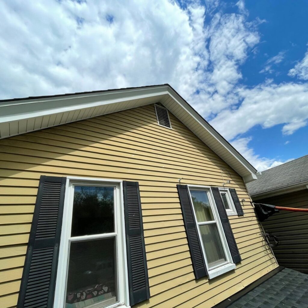 The yellow siding exterior of a house with black shutters, undergoing inspection or maintenance by Prescott Roofing and Masonry in Carnegie, PA.
