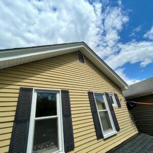 The yellow siding exterior of a house with black shutters, undergoing inspection or maintenance by Prescott Roofing and Masonry in Carnegie, PA.