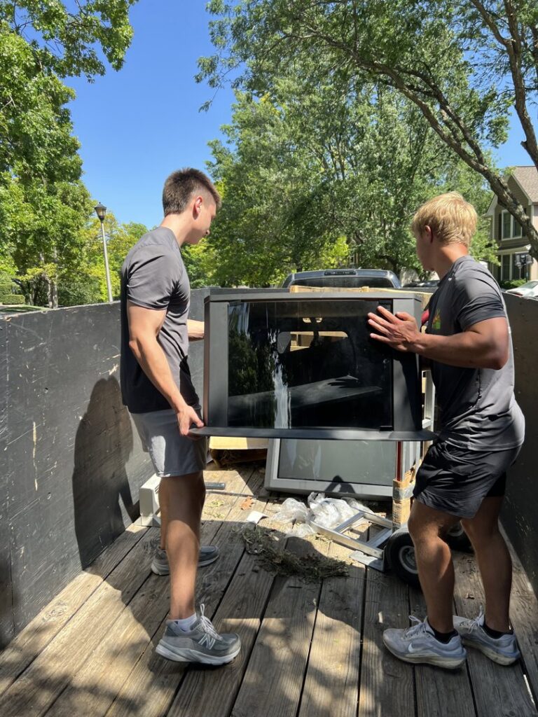 Two Young Bucks Junk employees loading a large window frame onto a trailer for removal in Shawnee, KS.