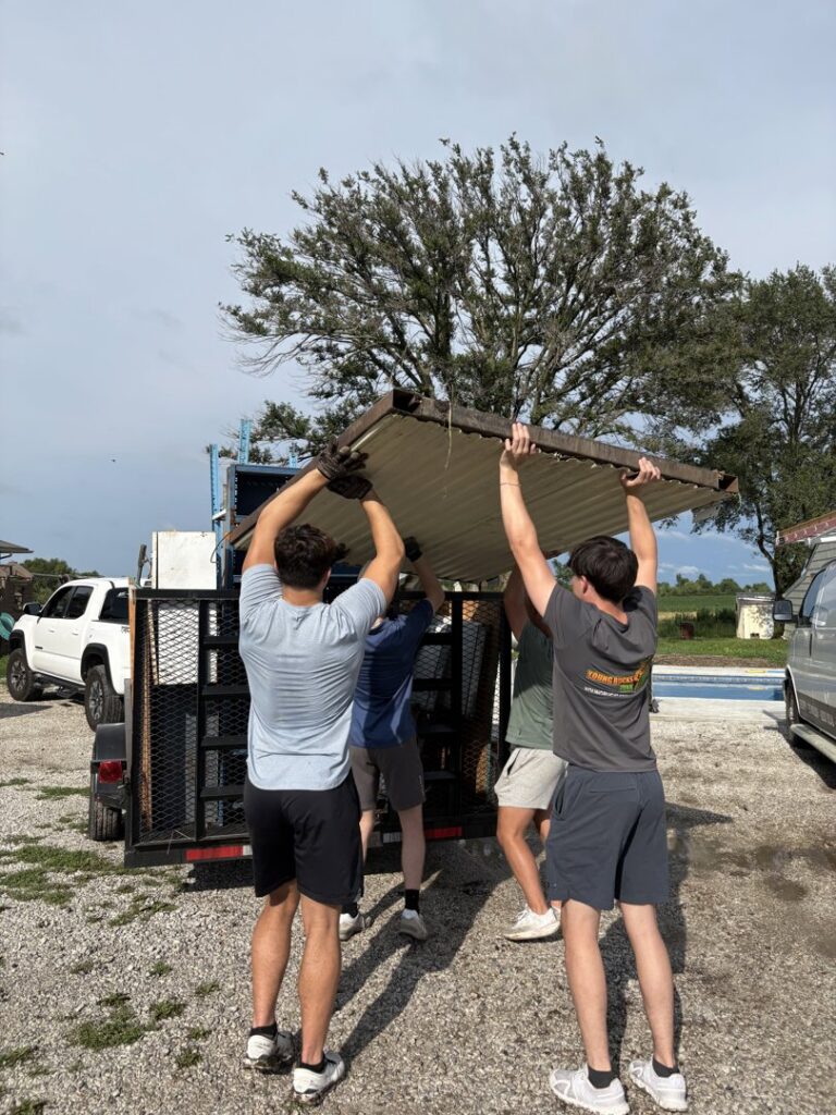 The Young Bucks Junk team carrying a large piece of corrugated metal towards a trailer for removal in Shawnee, KS.