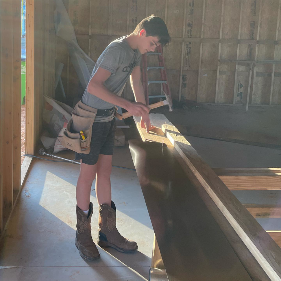 A young man wearing a tool belt working on wood framing at a construction site for Bryan Lee Builds in Oklahoma City, OK.