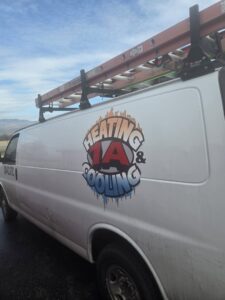 A white service van with the 1A Heating & Cooling Specialty LLc logo and ladders on the roof rack in Caldwell, ID.