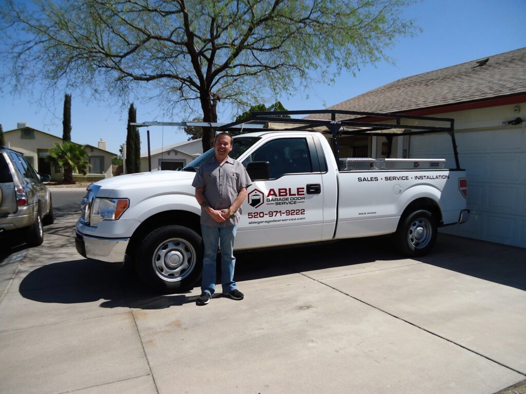 A technician from Able Garage Door Service, LLC standing next to a company service truck in Tucson, AZ.
