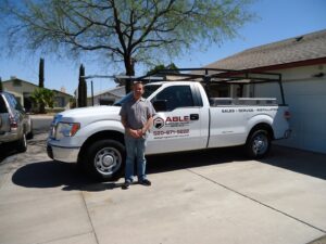 A technician from Able Garage Door Service, LLC standing next to a company service truck in Tucson, AZ.