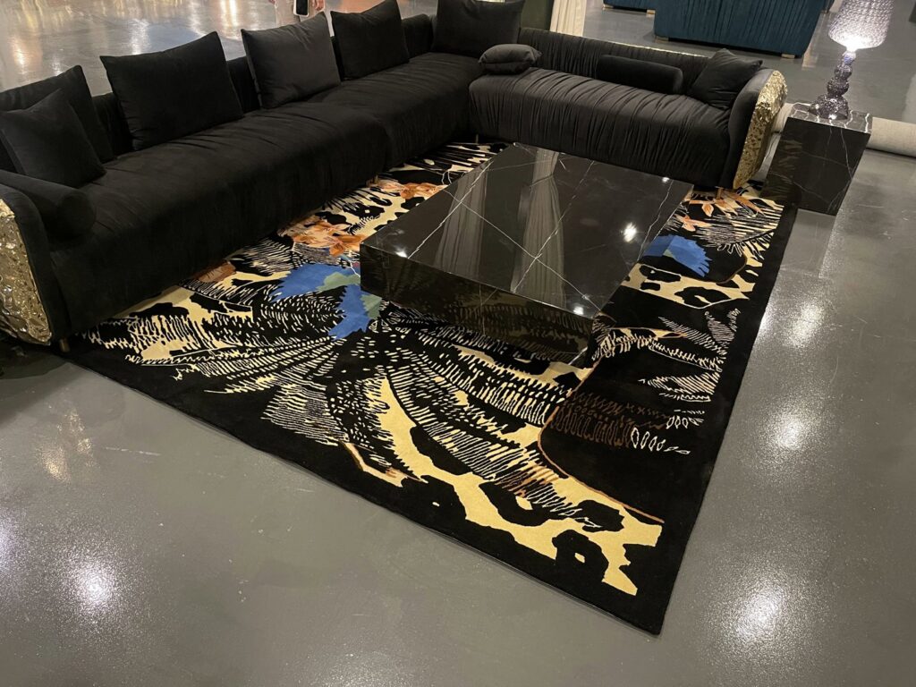 A large black rug with an abstract pattern displayed in a showroom setting with a black sectional sofa at Makymo in Commerce, CA