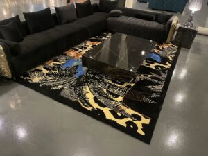 A large black rug with an abstract pattern displayed in a showroom setting with a black sectional sofa at Makymo in Commerce, CA
