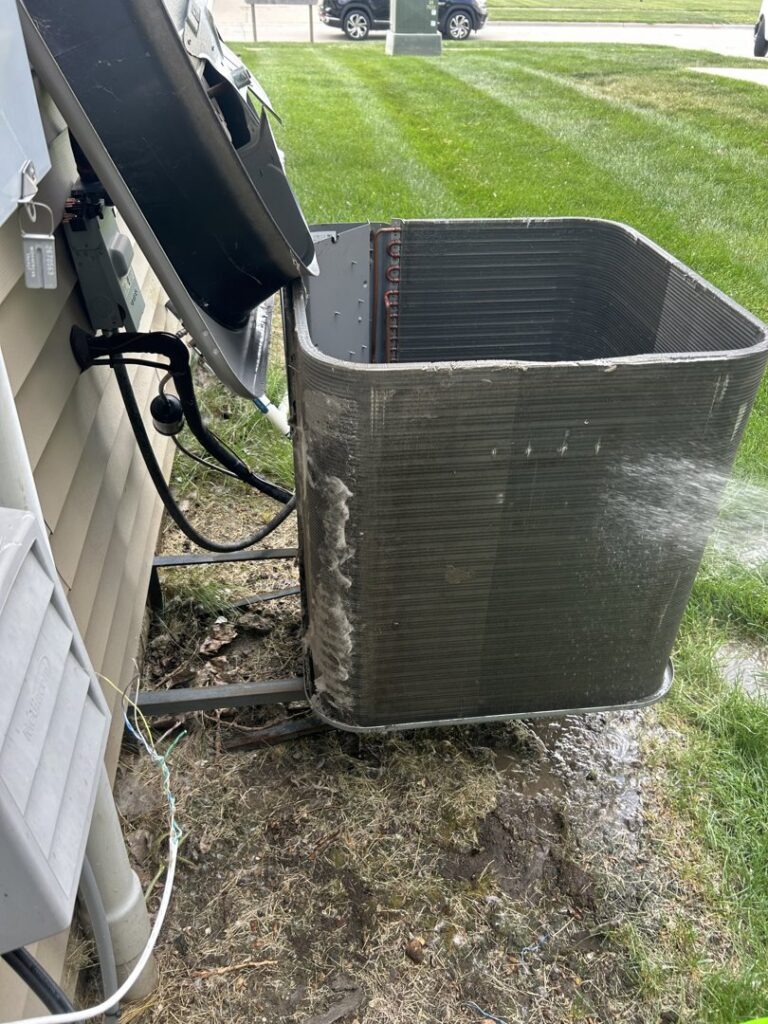 An outdoor AC condenser unit being professionally cleaned by Omega Air Solutions in West Des Moines, IA.