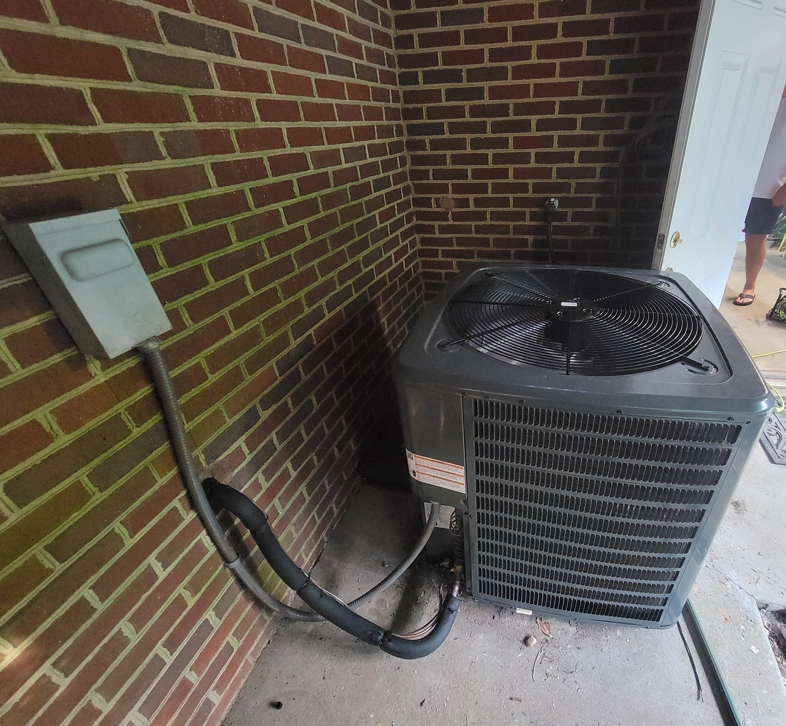 An AC condenser unit installed next to a brick wall with electrical connections by Smoky Mountain Ducts & Vents in New Market, TN.