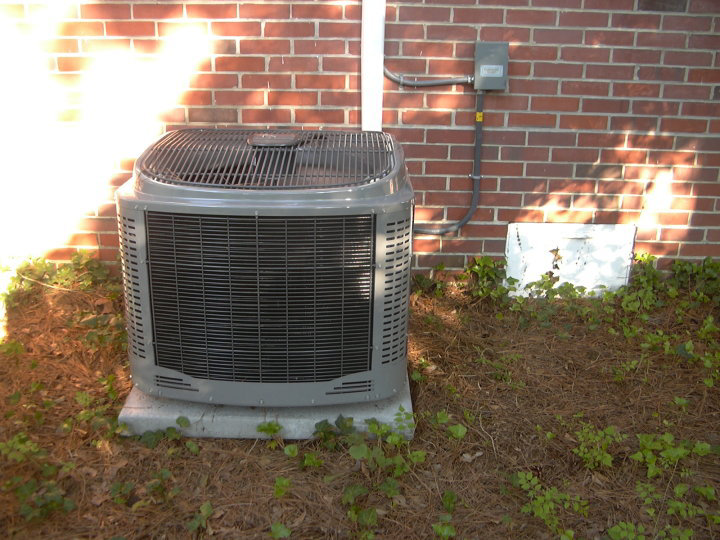 An outdoor AC condenser unit installed next to a brick house by Collis Mechanical Services in Norfolk, VA
