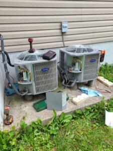 HVAC technician performing maintenance or repair on two outdoor Carrier AC units for Duct Pros in Martinsburg, WV