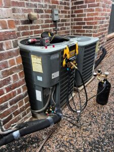 An outdoor AC unit undergoing refrigerant charging with gauges and tanks connected by Jupitair in Frisco, TX.