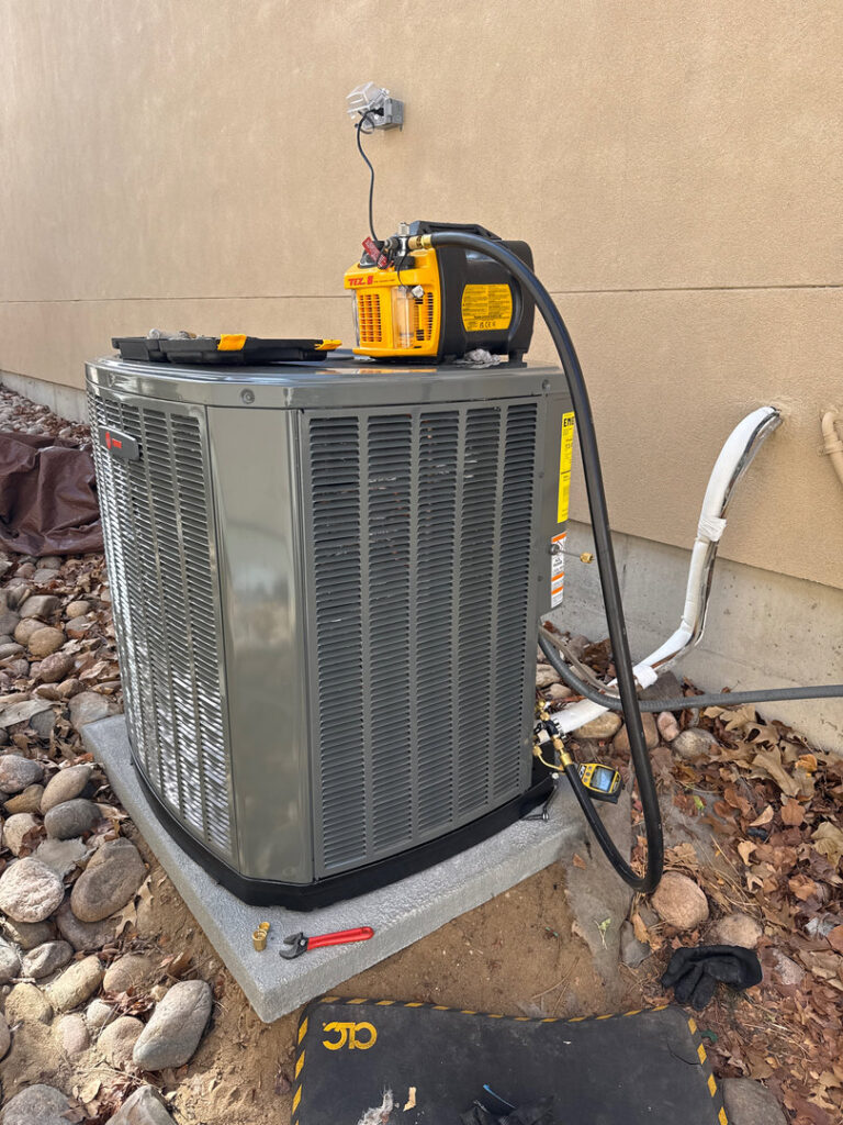 An outdoor AC unit undergoing refrigerant service with a vacuum pump and gauges by Primary Air Home Services in Aurora, CO.