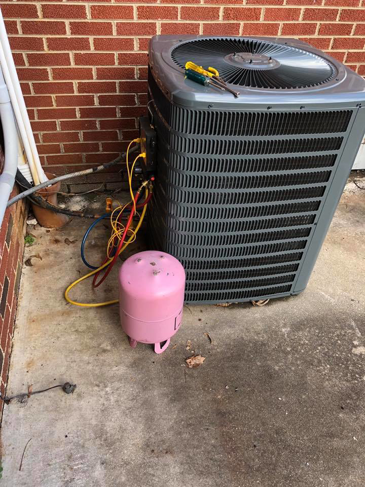 An outdoor air conditioning unit being serviced with a refrigerant tank by G&G Heating and Air in Portage, MI.