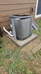 An outdoor AC unit with its side panel removed, showing coils, indicating service or repair by Erik's Quality HVAC LLC in Greeley, CO.