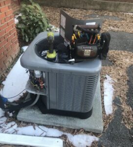 An outdoor air conditioning unit being serviced with tools on top, with some snow on the ground, by Climate Mechanical in Dinwiddie, VA.