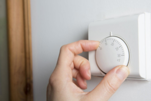 A hand adjusting a thermostat to control indoor temperature, a service related to Comfort First Heating & Cooling in Dewitt, MI.