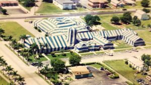 An aerial view of a large building complex covered in blue and white striped tarps for pest control fumigation by Shield Pest Control in Homestead, FL.
