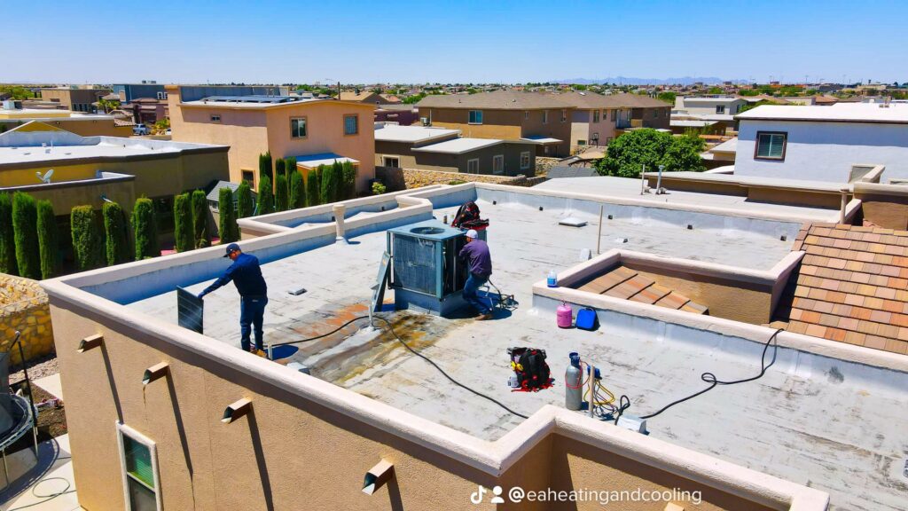 An aerial view of two HVAC technicians performing service on a rooftop unit for EA Heating & Cooling in El Paso, TX.