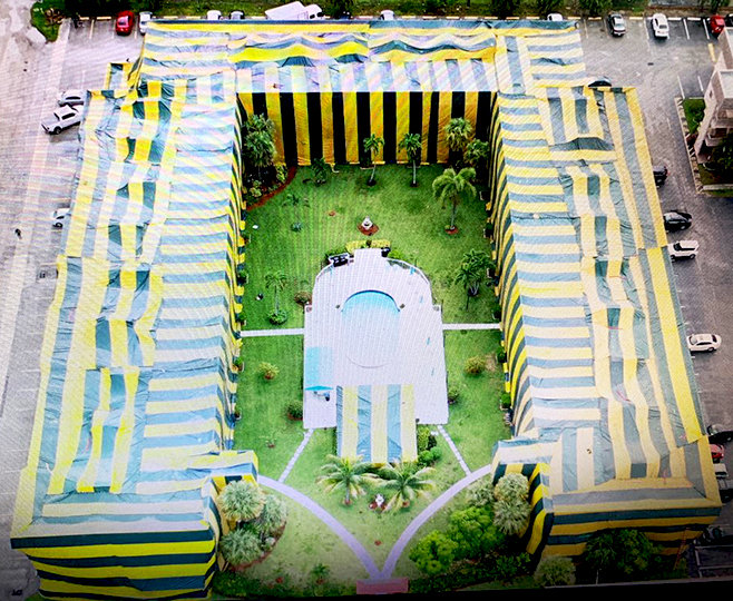 An aerial view of a large building complex covered in yellow and blue tarps for pest control fumigation by Shield Pest Control in Homestead, FL.