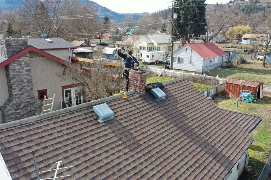 An aerial view of a Chimney Wizards LLC technician on a roof next to a chimney, performing service in Orofino, ID.