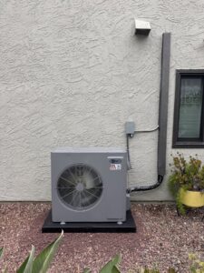 An Aero brand outdoor HVAC condenser unit installed on a gravel bed next to a house by Pelican Heating and Air in Carlsbad, CA.
