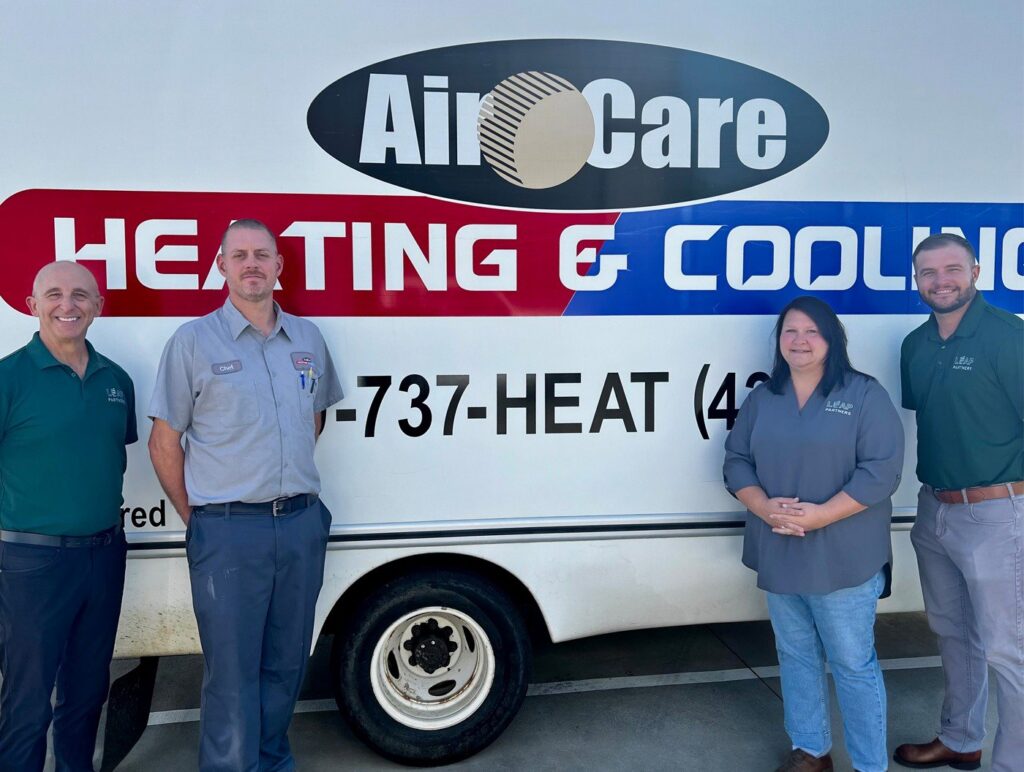 Four members of the Air Care Heating & Cooling team standing by their service van for Leap Partners in Greensboro, NC.