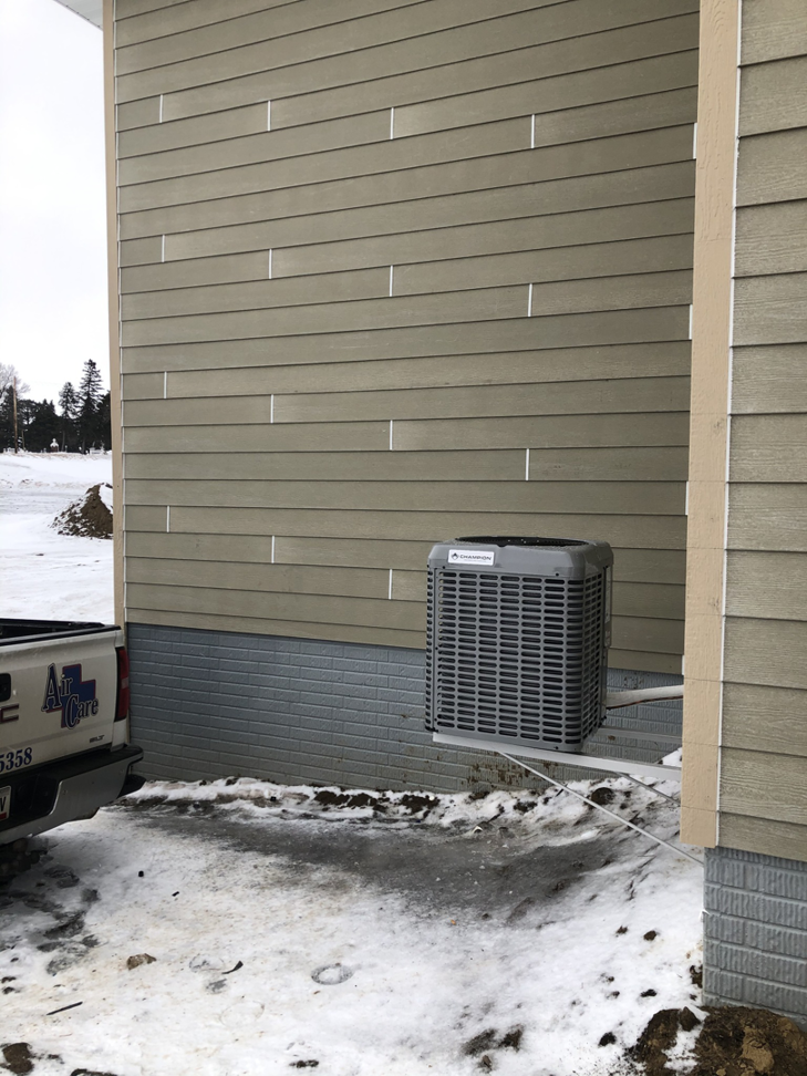 An Air Care service truck next to a mounted outdoor AC unit installation in a winter setting in Sioux Falls, SD.