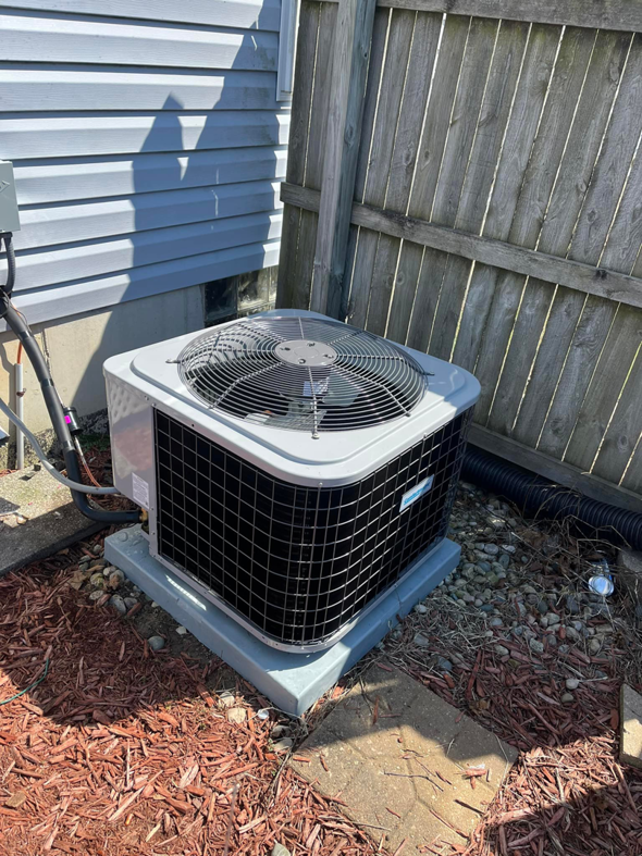 An air conditioning unit installed on a concrete pad next to a house with siding by Motown Mechanical Heating And Cooling in Westland, MI.