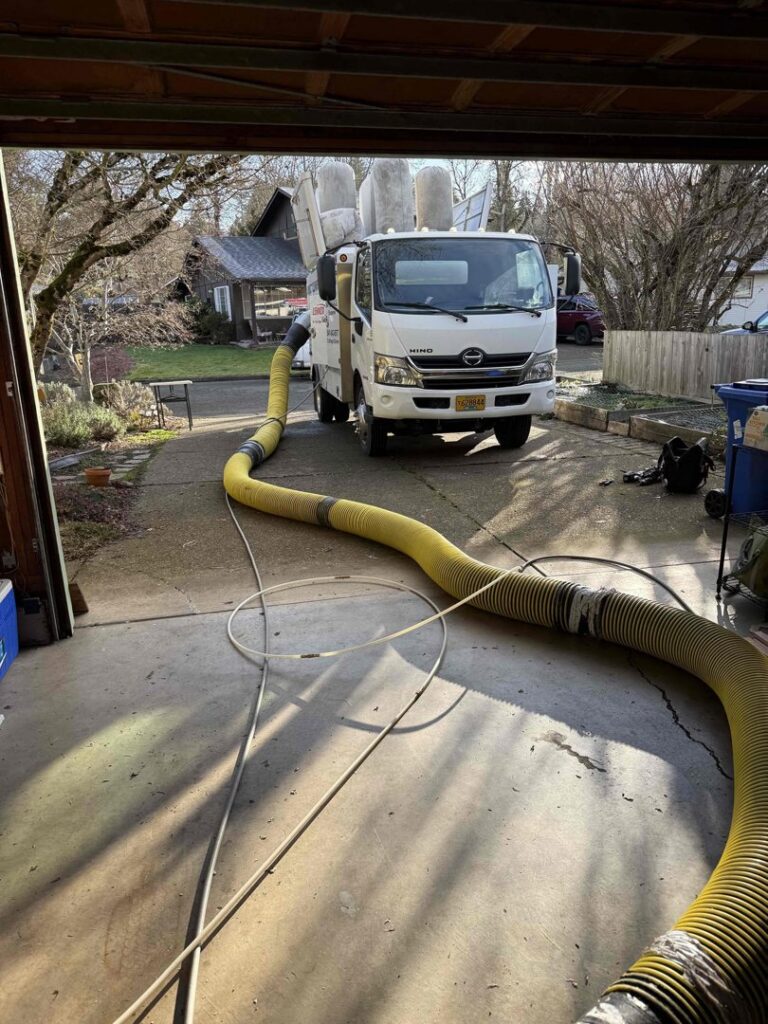 An Alpine Heating air duct cleaning service truck with a hose extending into a garage in Eugene, OR.