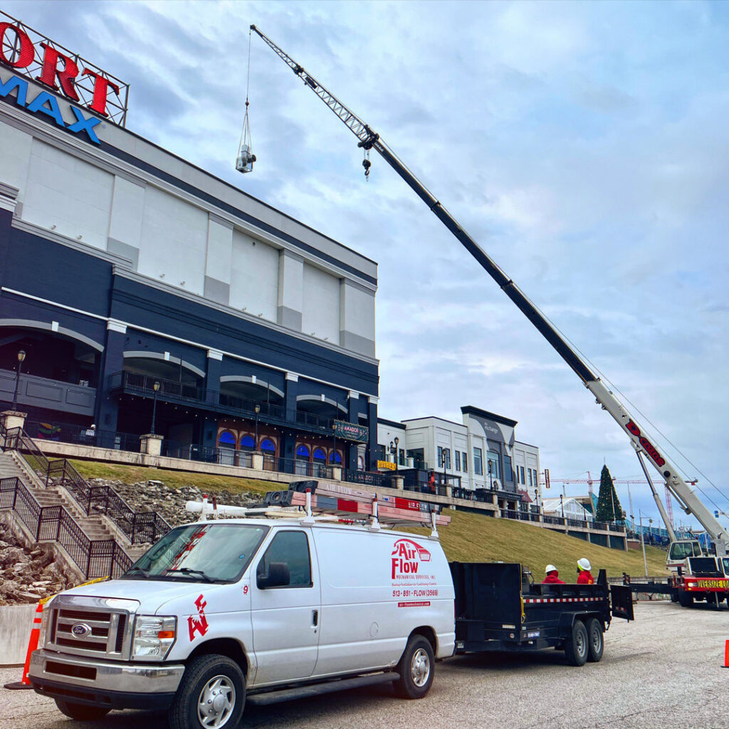 An Air-Flow Mechanical Services, Inc. van and trailer at a commercial HVAC job site with a crane lifting equipment in Cincinnati, OH.