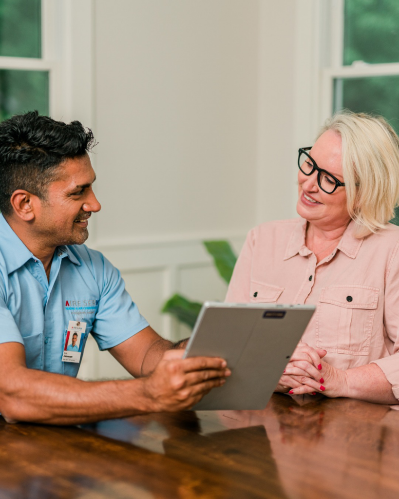 An Aire Serv technician consulting with a female customer, showing information on a tablet in Billings, MT.