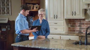 An Aire Serv technician consulting with a female customer in a kitchen, showing information on a tablet in Billings, MT.