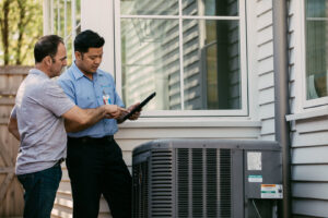 An Aire Serv technician discussing an outdoor AC unit with a customer, showing information on a tablet in Billings, MT.