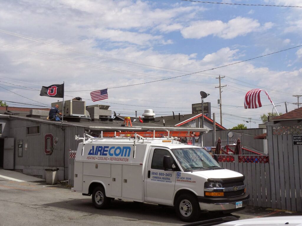 An AireCom HVAC service van parked at a job site with a technician on the roof in Columbus, OH.