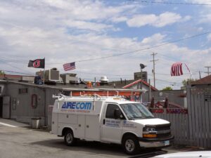 An AireCom HVAC service van parked at a job site with a technician on the roof in Columbus, OH.