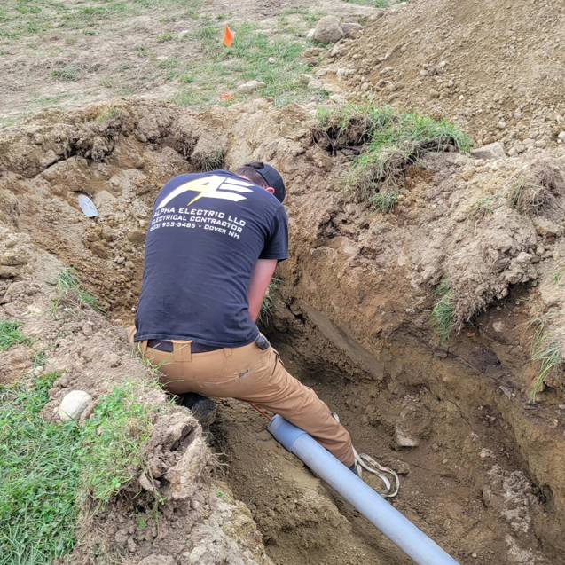 An Alpha Electric LLC electrician installing underground electrical conduit in a trench in Dover, NH.
