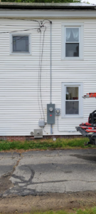 A residential electrical service entrance with meter and conduit on a building, installed by Alpha Electric LLC in Dover, NH.