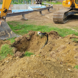 Underground electrical cables in an excavated trench with an excavator nearby, handled by Alpha Electric LLC in Dover, NH.