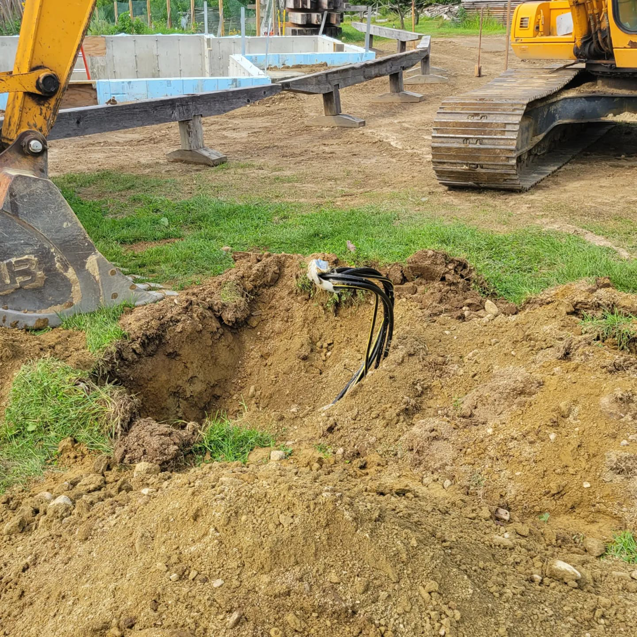 Underground electrical cables in an excavated trench with an excavator nearby, handled by Alpha Electric LLC in Dover, NH.