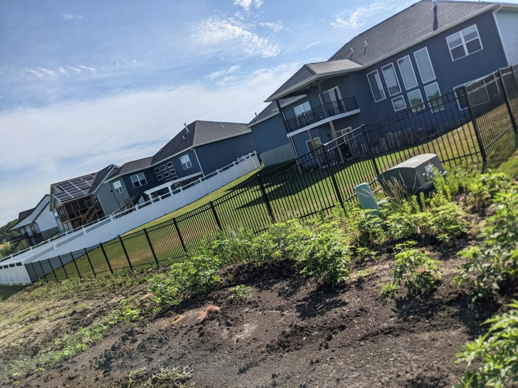 Black ornamental aluminum and white vinyl fences installed on a sloped residential property by Corridor Residential Fencing Co. in Cedar Rapids, IA.