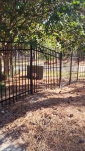 A black aluminum fence with a gate installed in a natural, wooded setting by Aguilarfence services LLC in Clayton, NC.